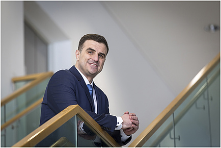 A man leaning on a handrail smiles into the camera