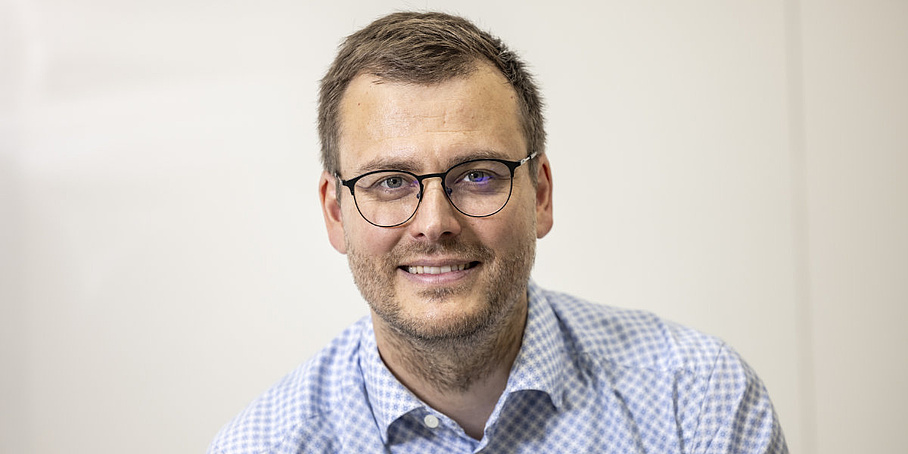 A man wearing glasses looks at the camera and smiles.