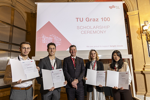 Five people stand next to each other and look into the camera, four of them holding certificates in their hands.