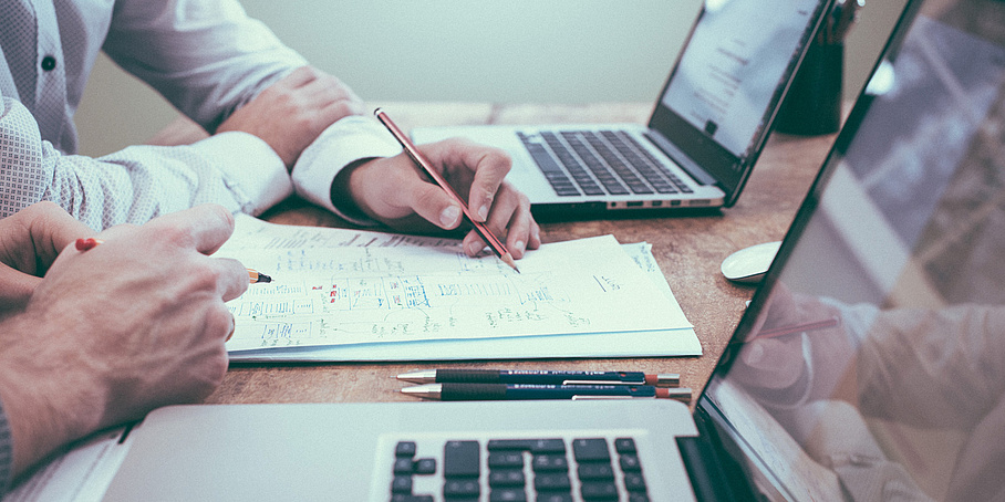 zwei Personen arbeiten gemeinsam an einem Schreibtisch mit Laptops und Papier