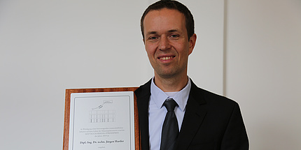 A man wearing a suit is smiling at the camera. He caries a certificate.