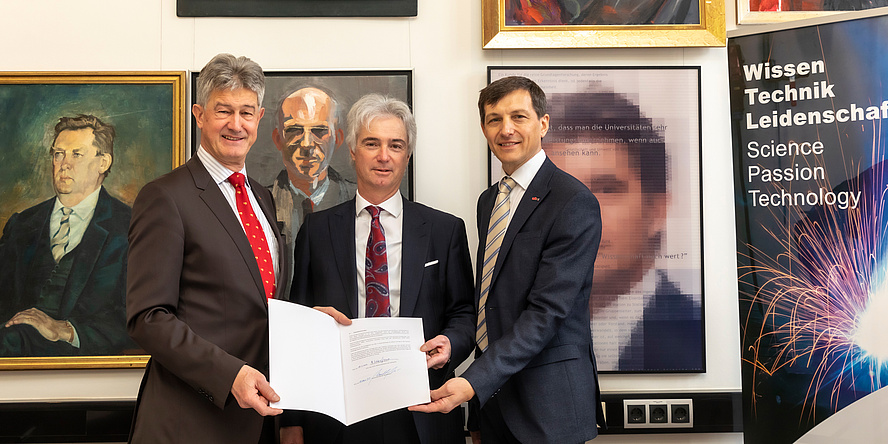 Three men in suits hold up a signed contract to the camera