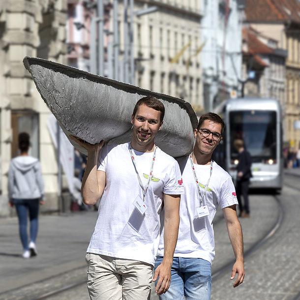 Zwei Männer tragen ein Betonkanu durch die Stadt.
