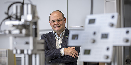 A man is standing in a laboratory with his arms folded, looking into the camera.