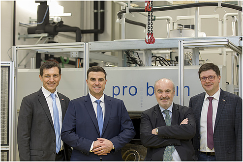 Four men stand smiling in front of a machine.