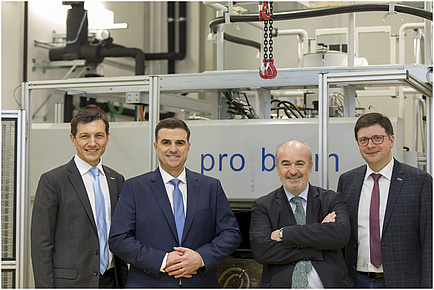 Four men stand smiling in front of a machine.