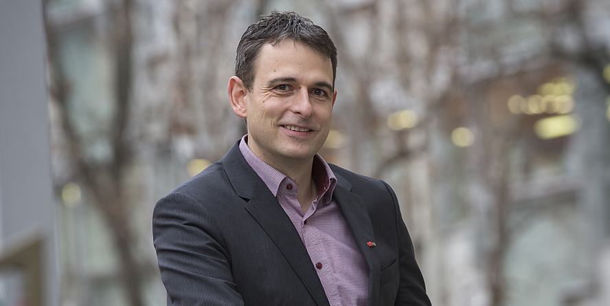 A man in a suit is standing in front of trees.