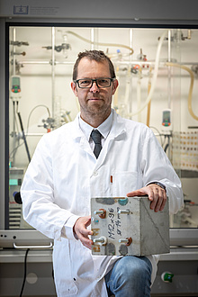 Researcher in white coat with concrete block in hands
