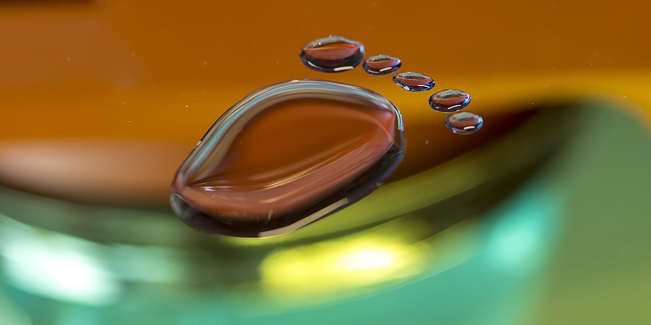 Ein durchsichtiger Fuß aus Flüssigkeit liegt auf einer orangen und grünen Oberfläche.