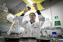 Man in laboratory coat swings glass flask with liquid.