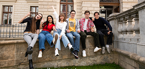Sechs Personen sitzen nebeneinander auf einer Mauer.