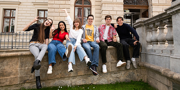 Sechs Personen sitzen nebeneinander auf einer Mauer.