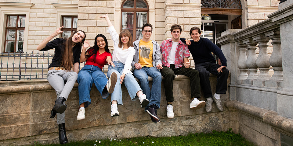 Sechs Personen sitzen nebeneinander auf einer Mauer.