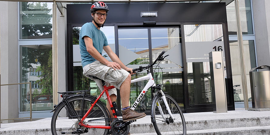 Ein Mann sitzt auf einem Fahrrad, das mit dem TU Graz-Logo versehen ist.