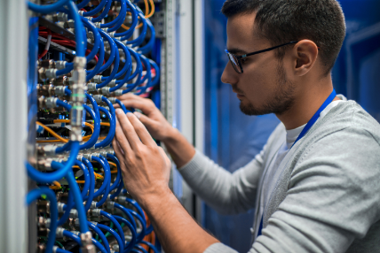 A manis working on a server rack in a data center. He is carefully adjusting and inspecting cables of various colors. 