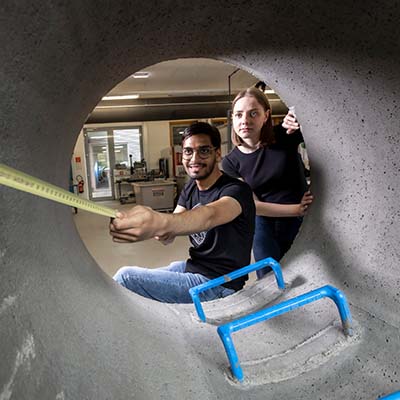 Zwei Studierende in einem Betonrohr messen mit dem Zollstock etwas ab. 