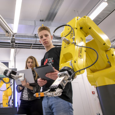 Eine Frau und ein Mann stehen neben einem Roboterarm. 
