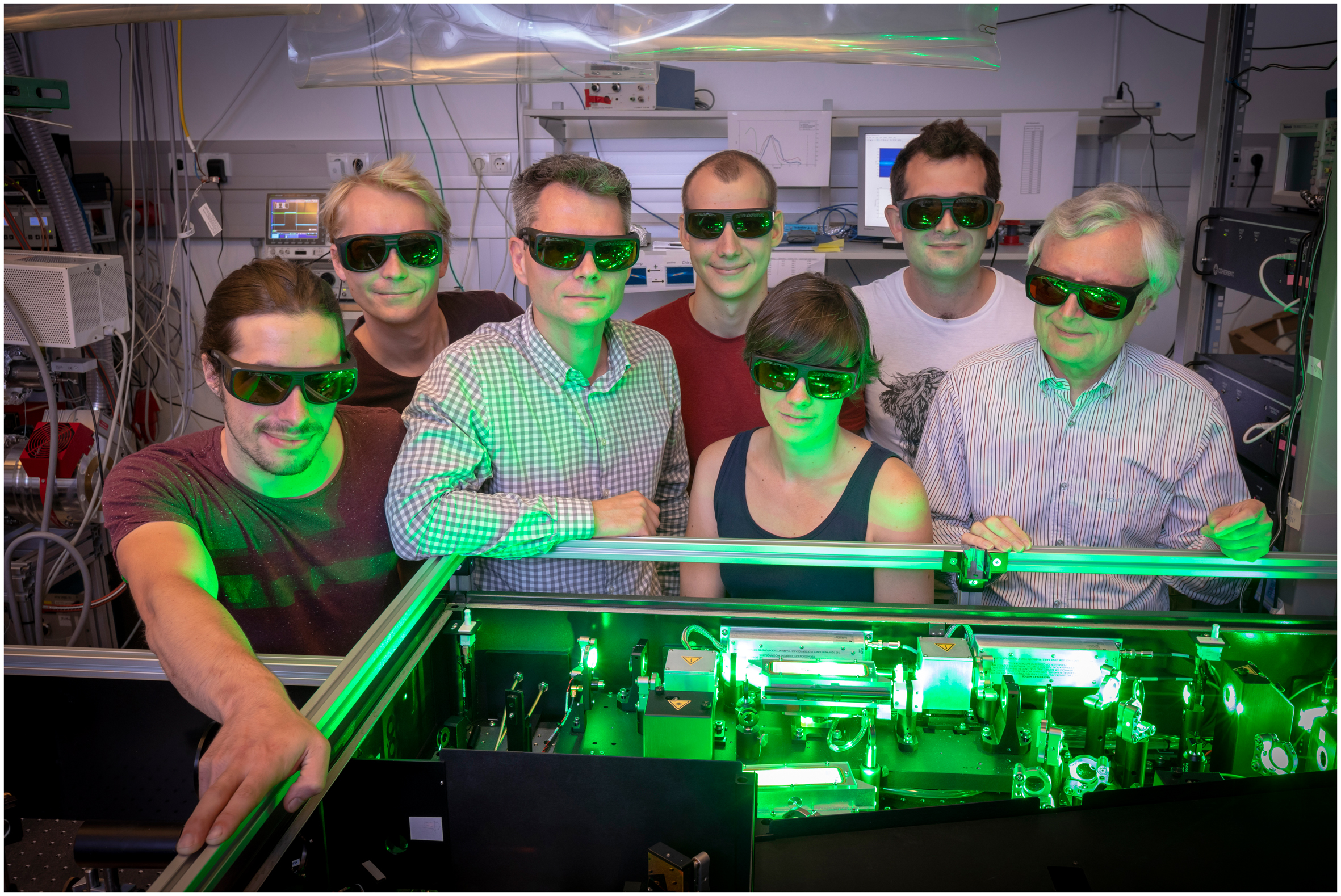 A group of researchers in the physics laboratory bathed in green light