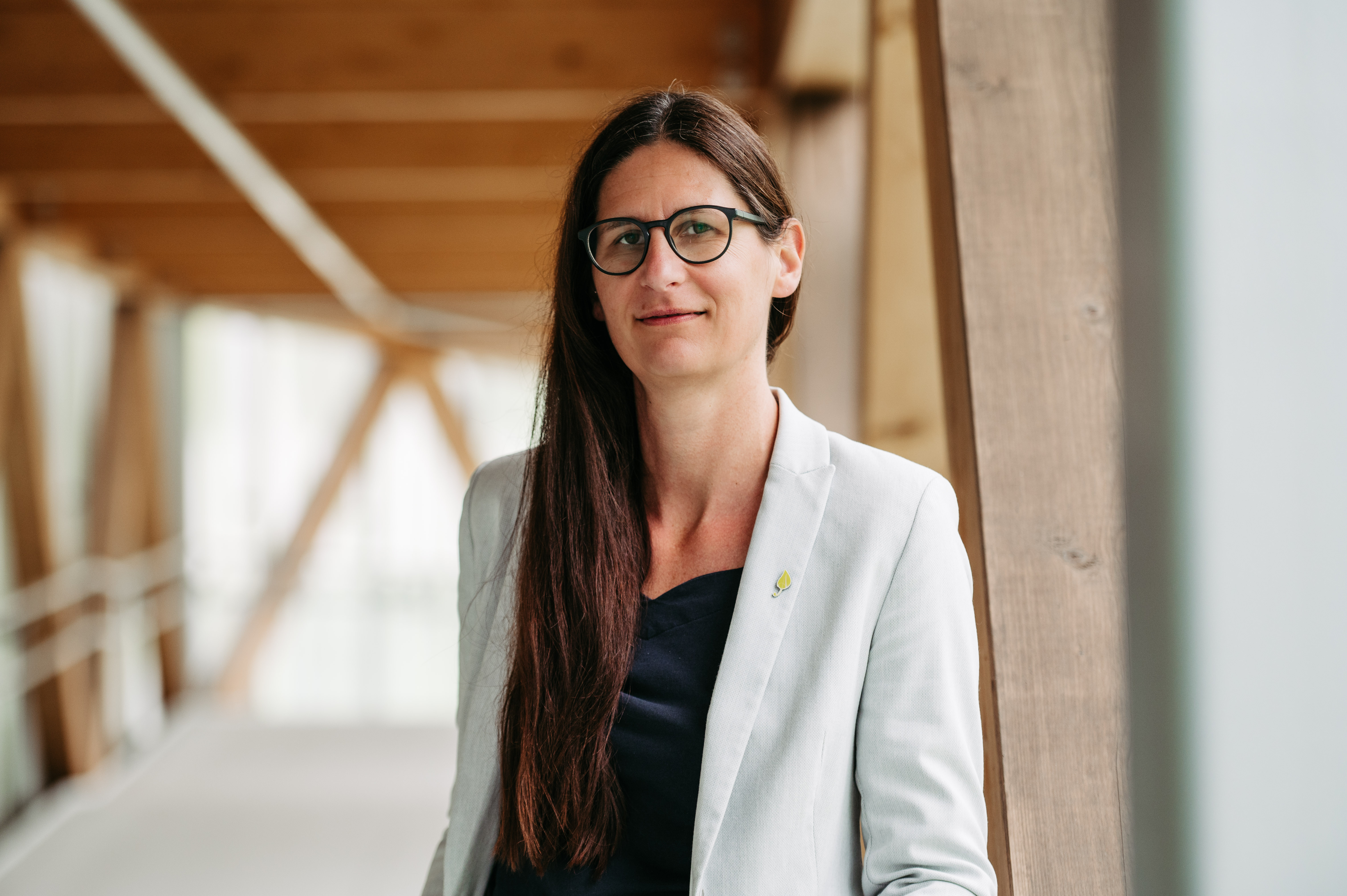Eine Frau mit Brille und weißem Sakko blickt in die Kamera.