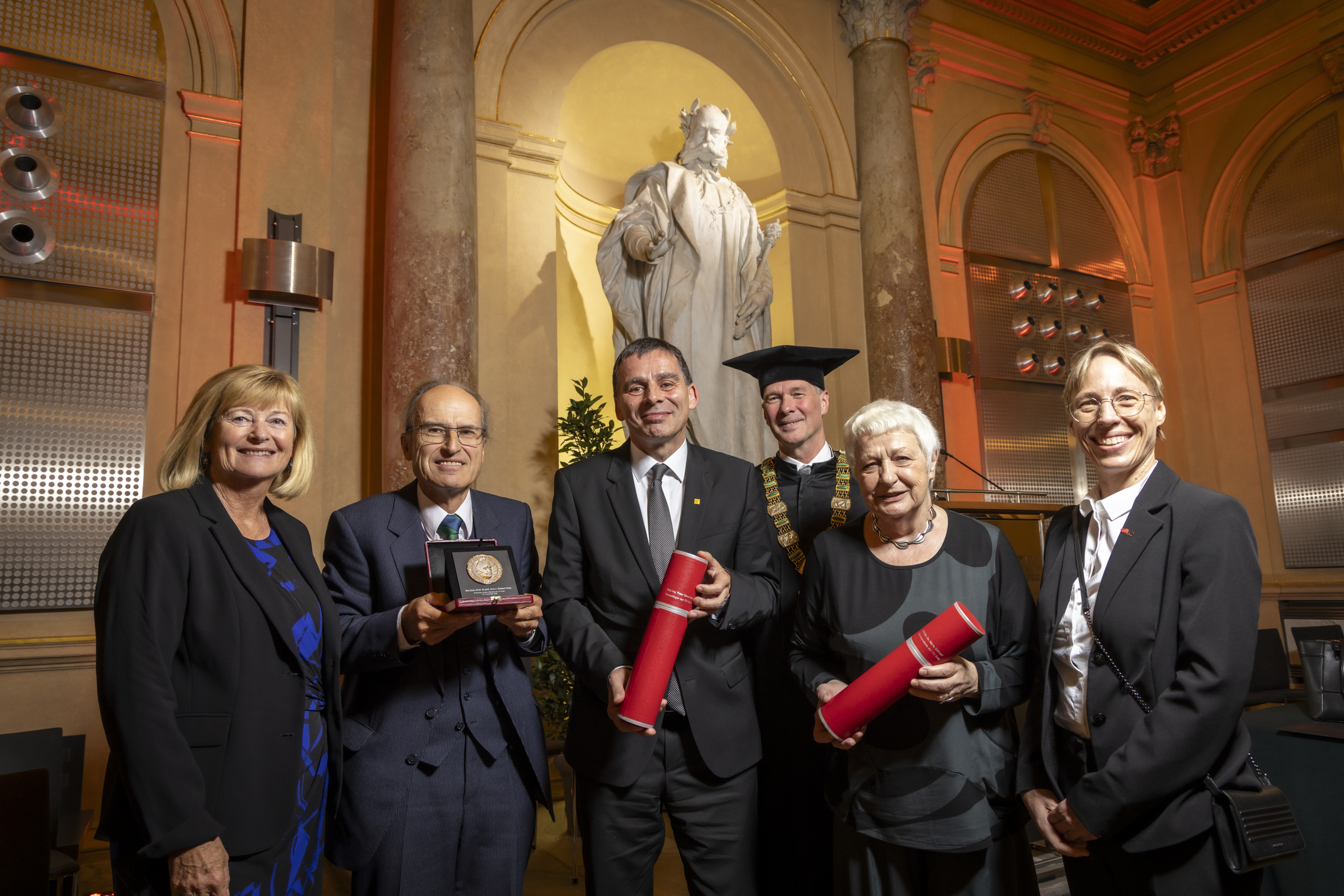 Eine Gruppe von sechs Personen, zwei davon mit Urkundenrollen in der Hand und eine mit einer Medaille in einer Schatulle.