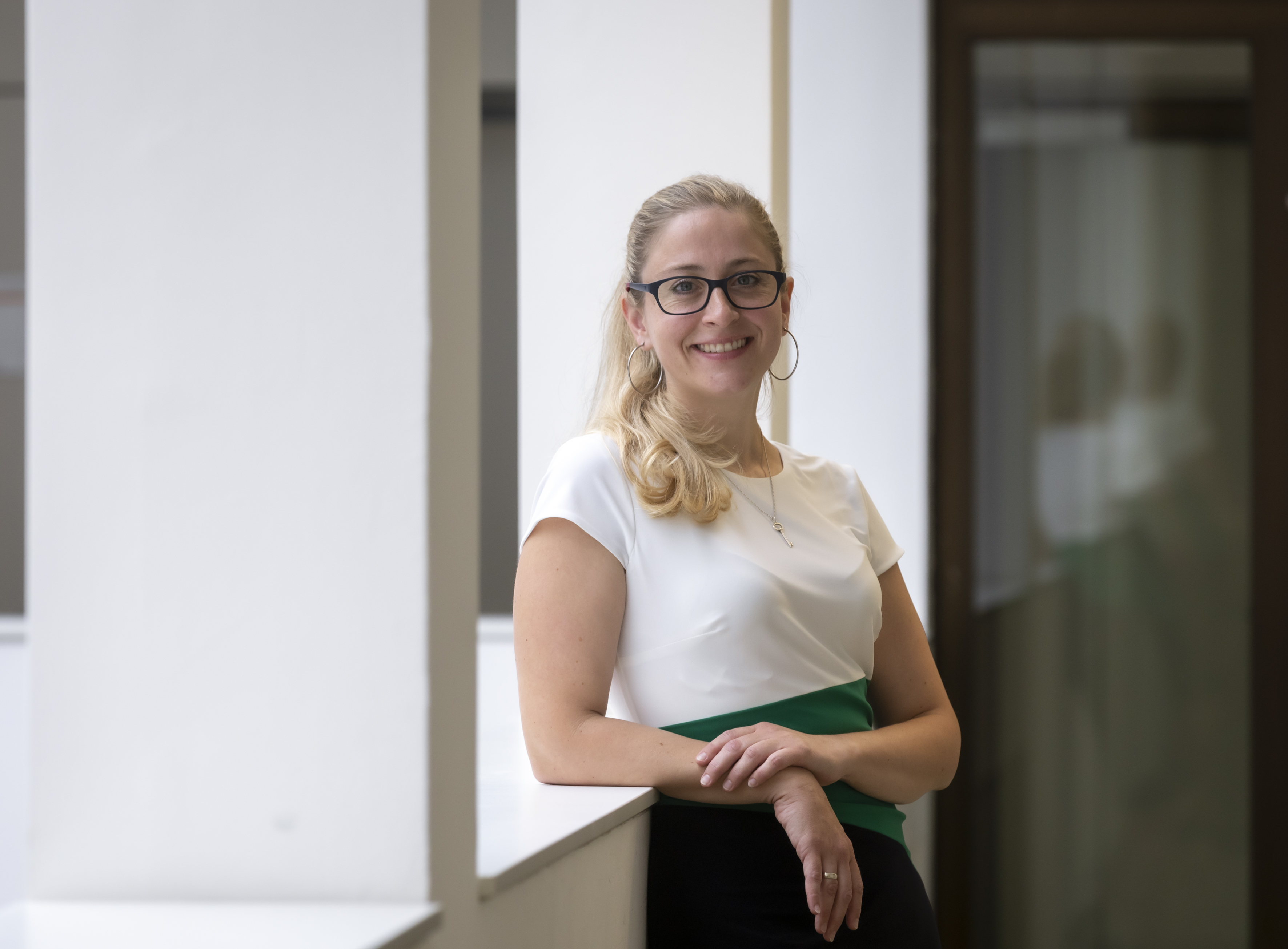 A woman with glasses leans against a balustrade and looks into the camera.