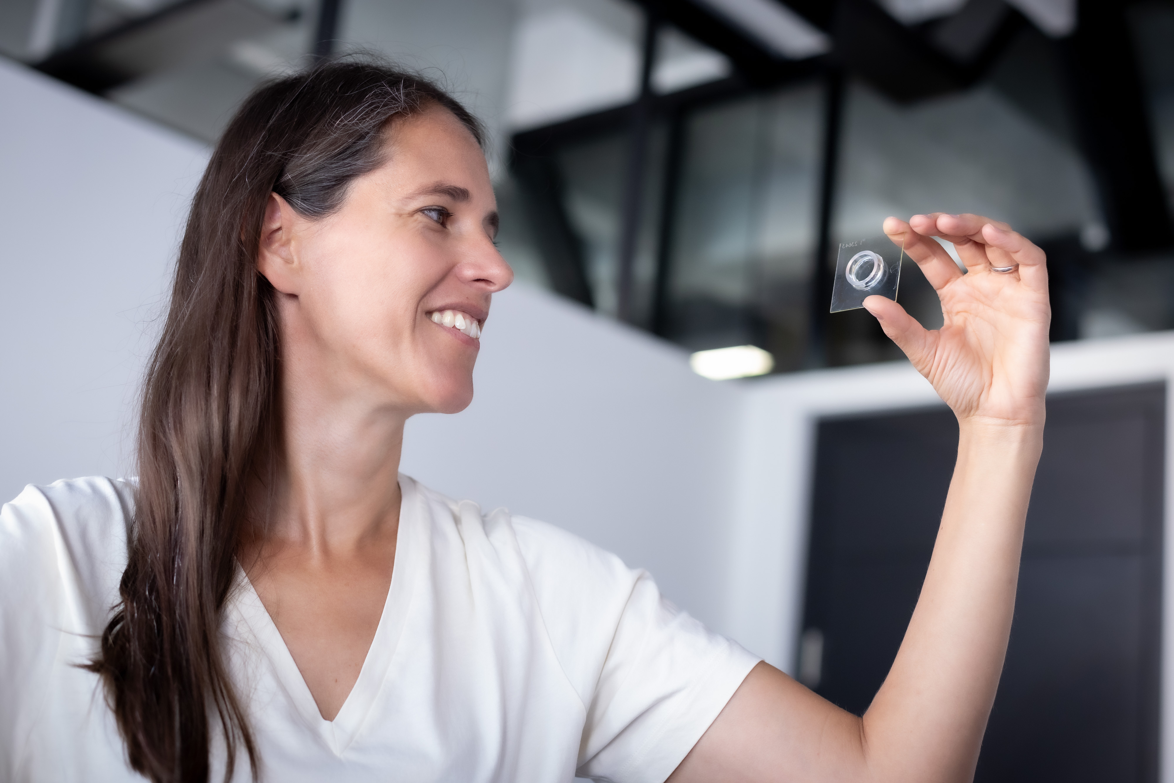 A woman is holding up a small glass plate and looks at it.