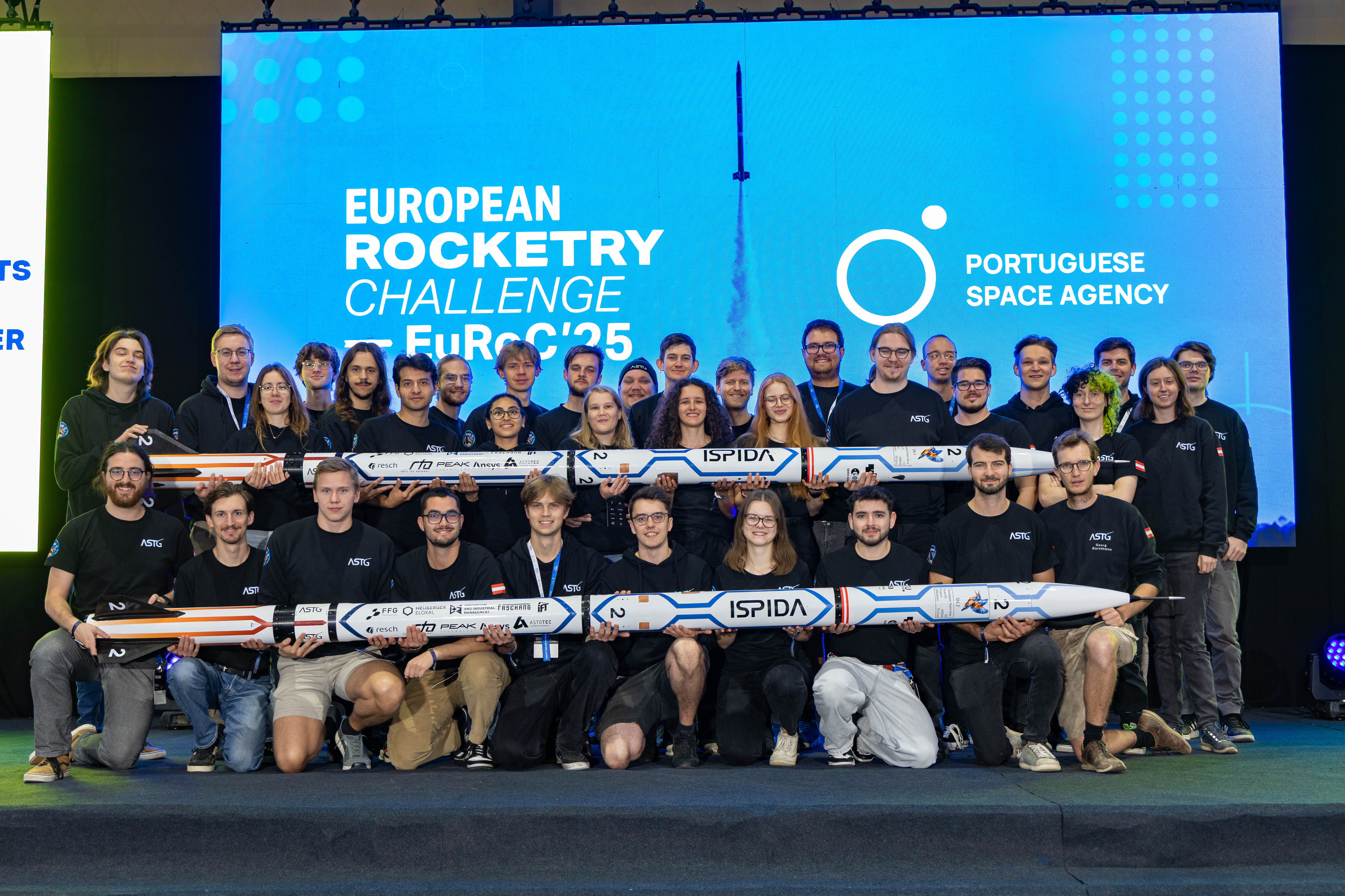 Das erfolgreiche Aerospace Team Graz. Bildquelle: ASTG Eine große Gruppe von Menschen steht in zwei Reihen hintereinander. Die vordere und die hintere Reihe hält jeweils eine Rakete vor sich.