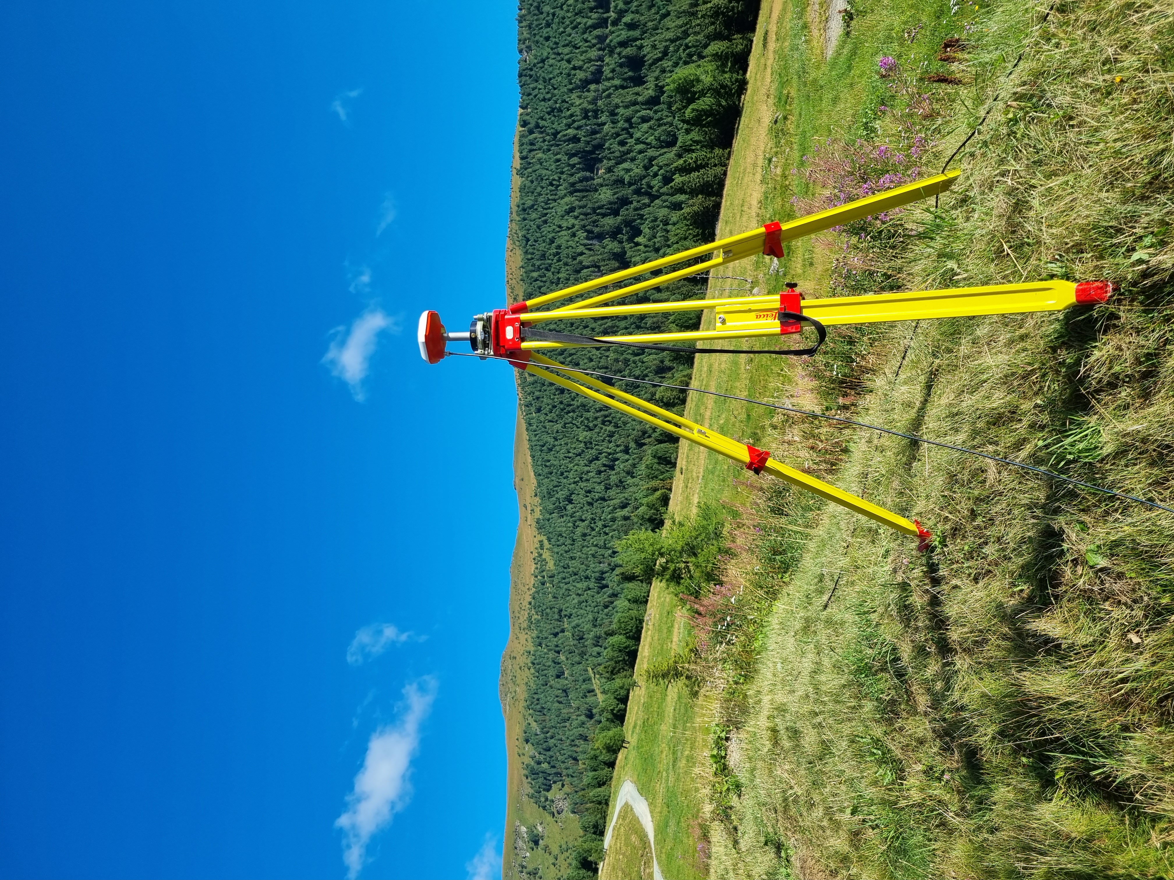 Eine GNSS-Antenne steht auf einer Wiese vor blauem Himmel.