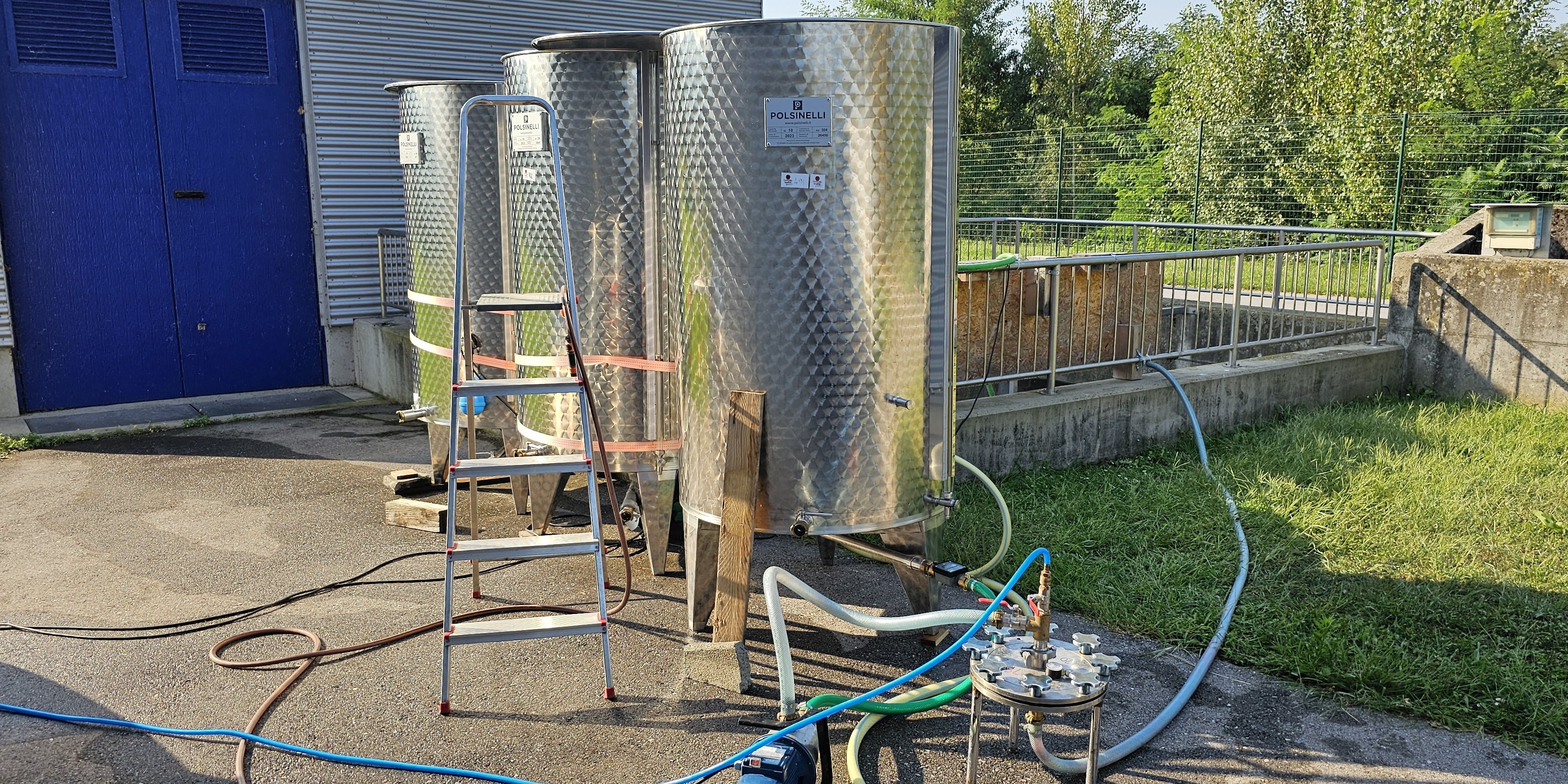 Drei Stahlbehälter, in die Schläuche hinein führen. Schräg davor steht eine Leiter.