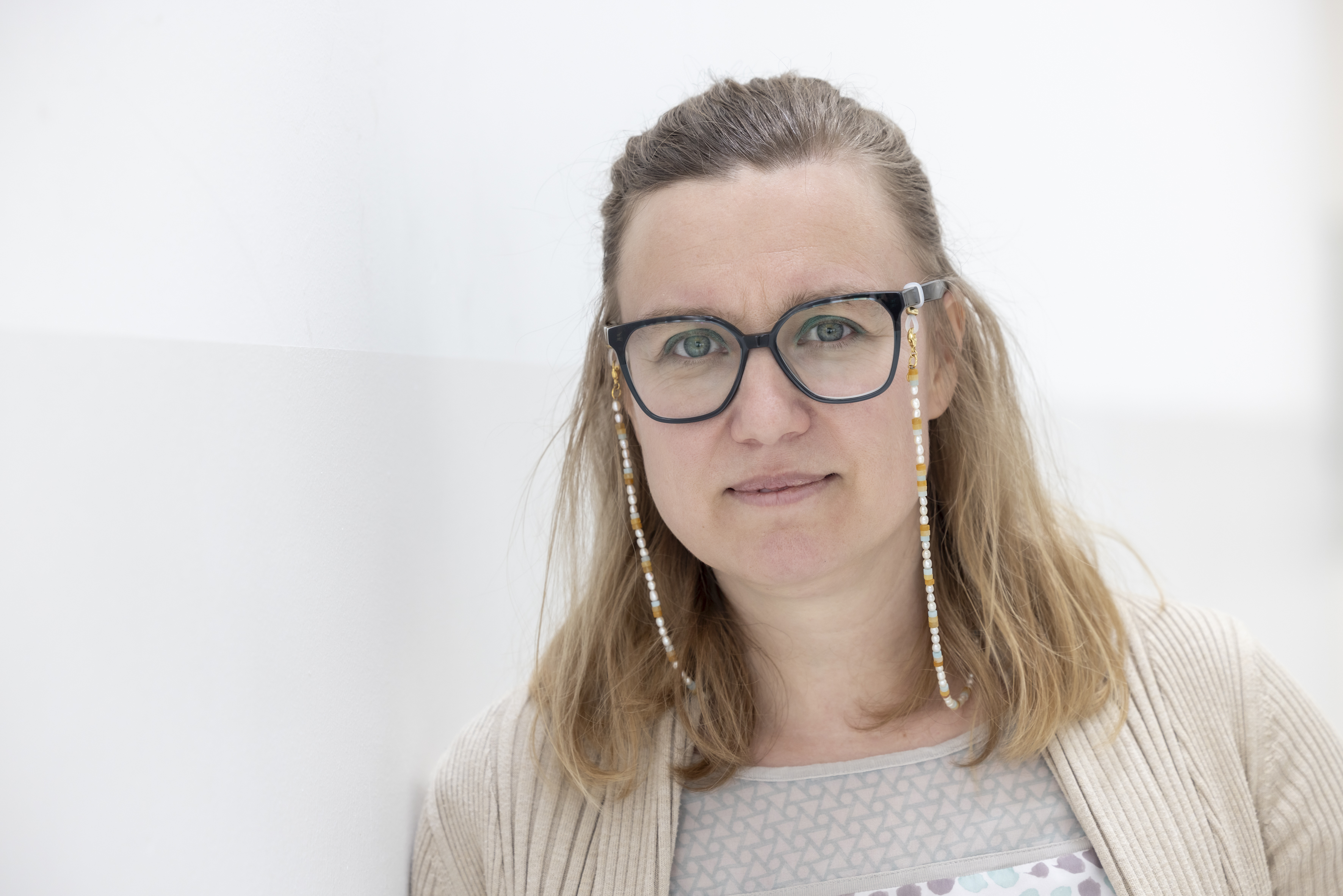 Eine Frau lehnt an einer Wand und schaut in die Kamera.
