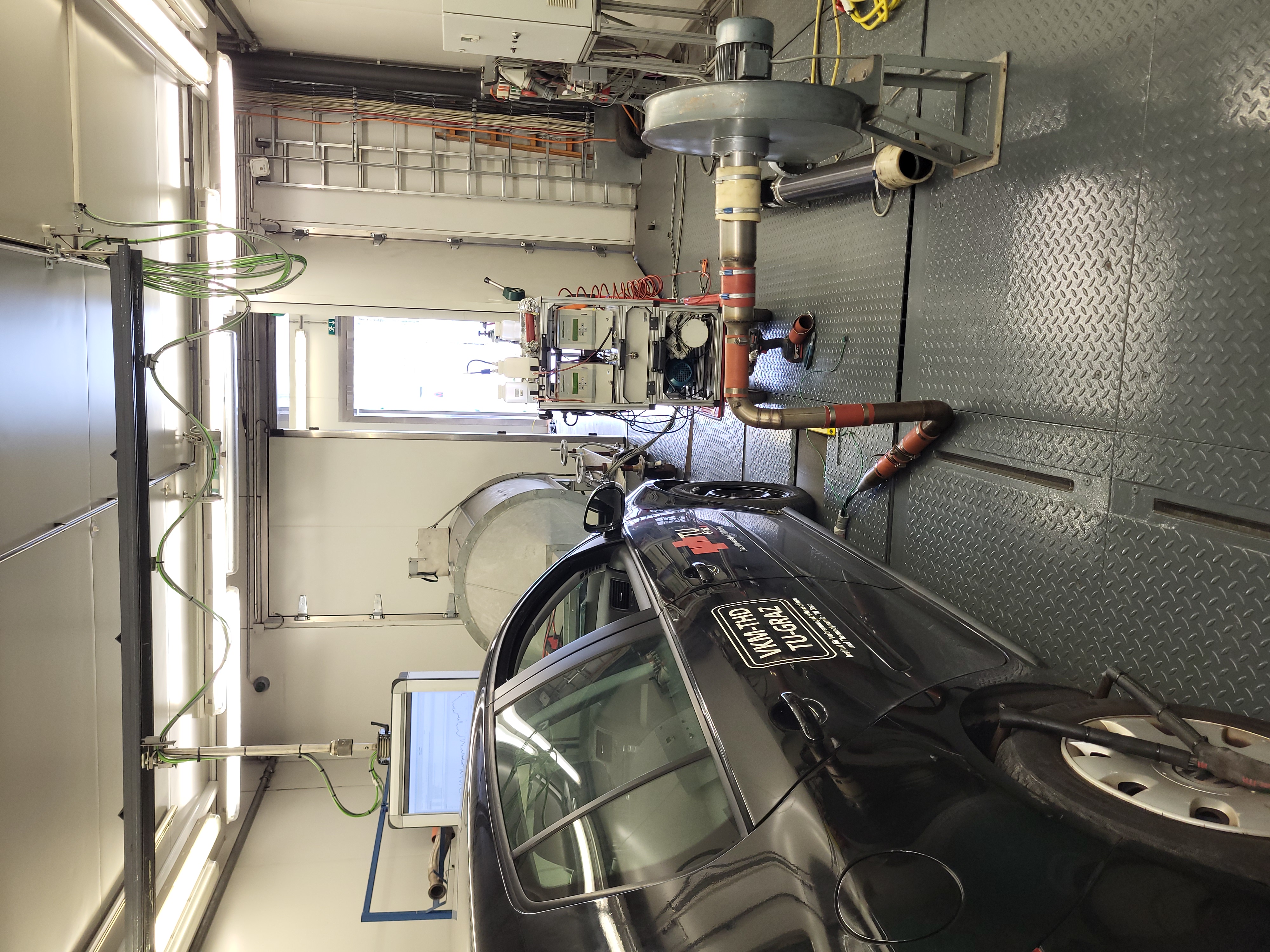 Foto von einem Auto auf einem Prüfstand im inneren einer kleinen Halle.