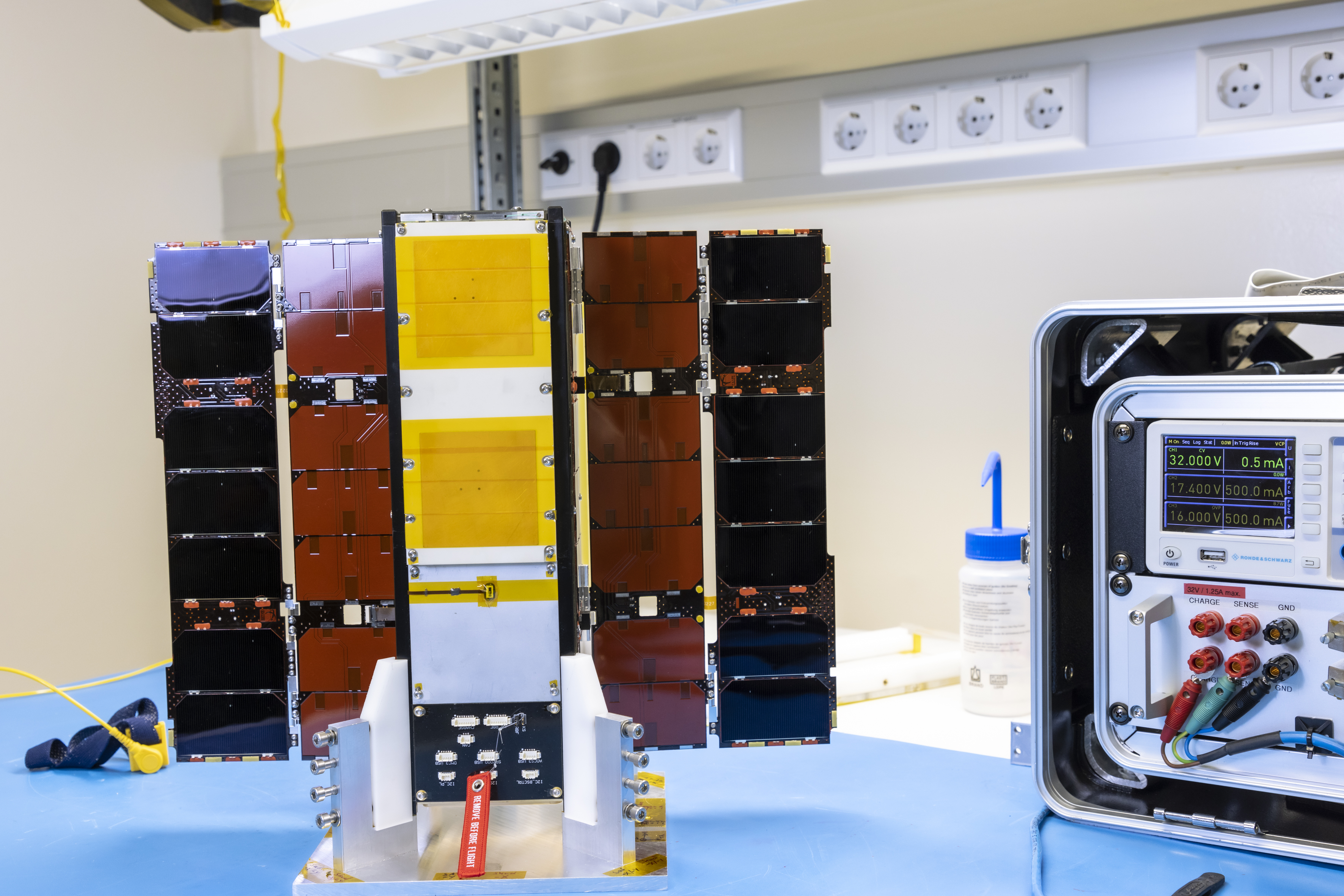 Ein kleiner Satellit mit ausgeklappten Sonnensegeln steht auf einem Tisch.