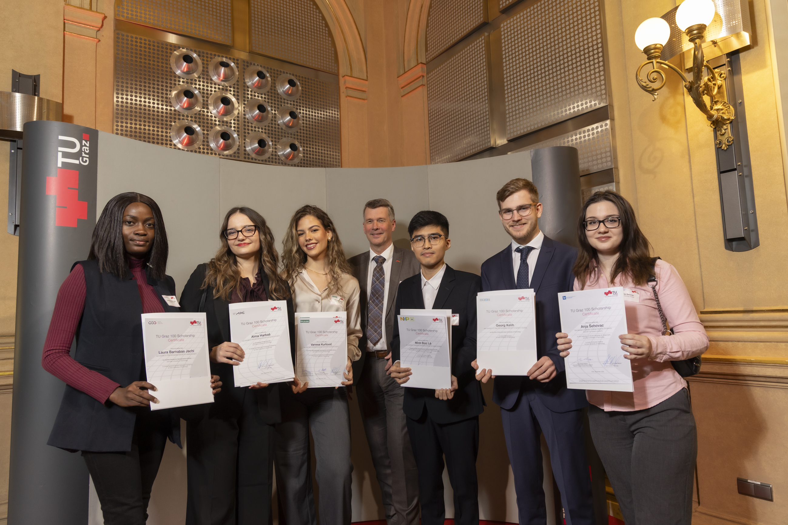 Seven people stand next to each other, holding certificates in their hands and looking at the camera.