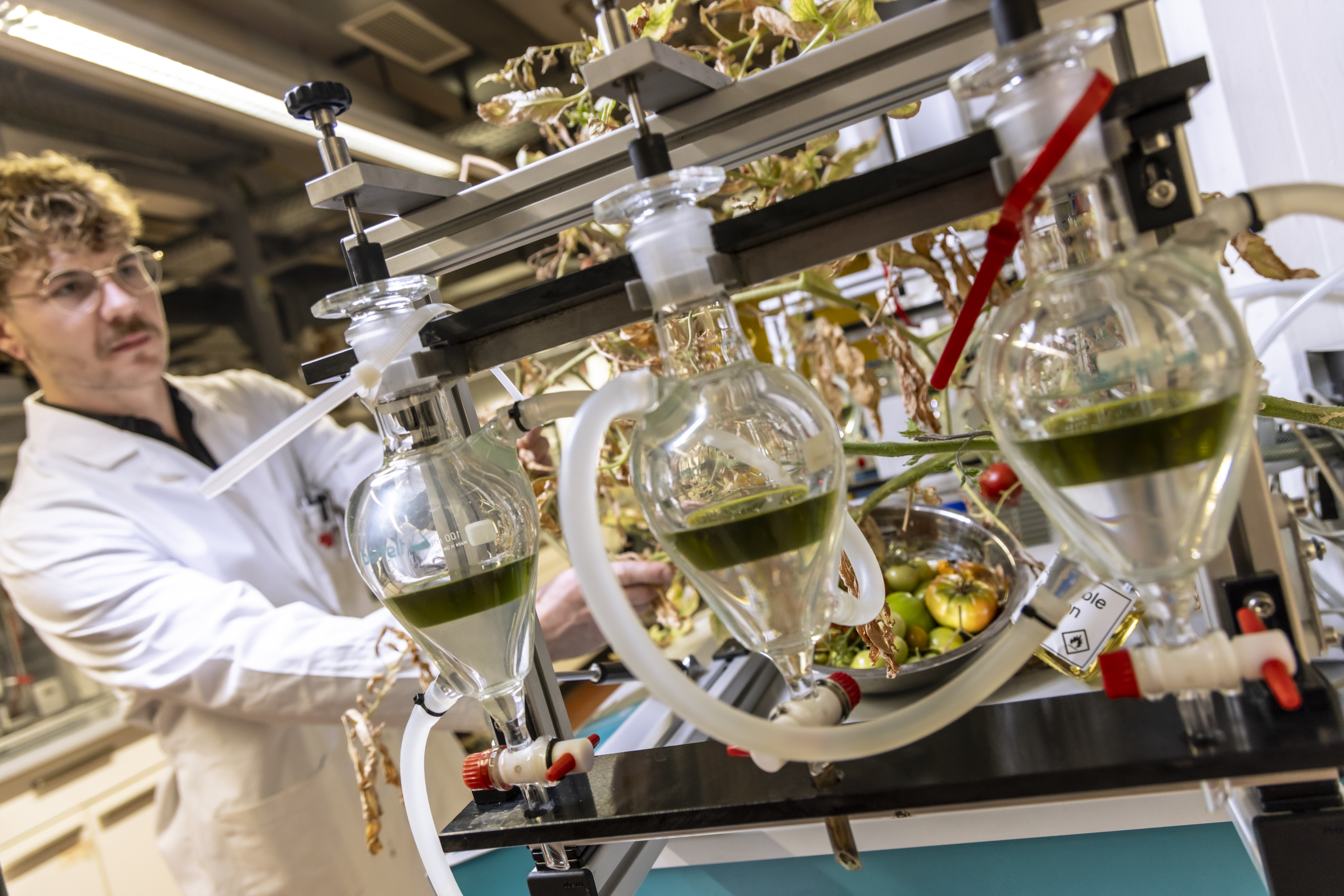 Man in a lab coat next to glass apparatus.