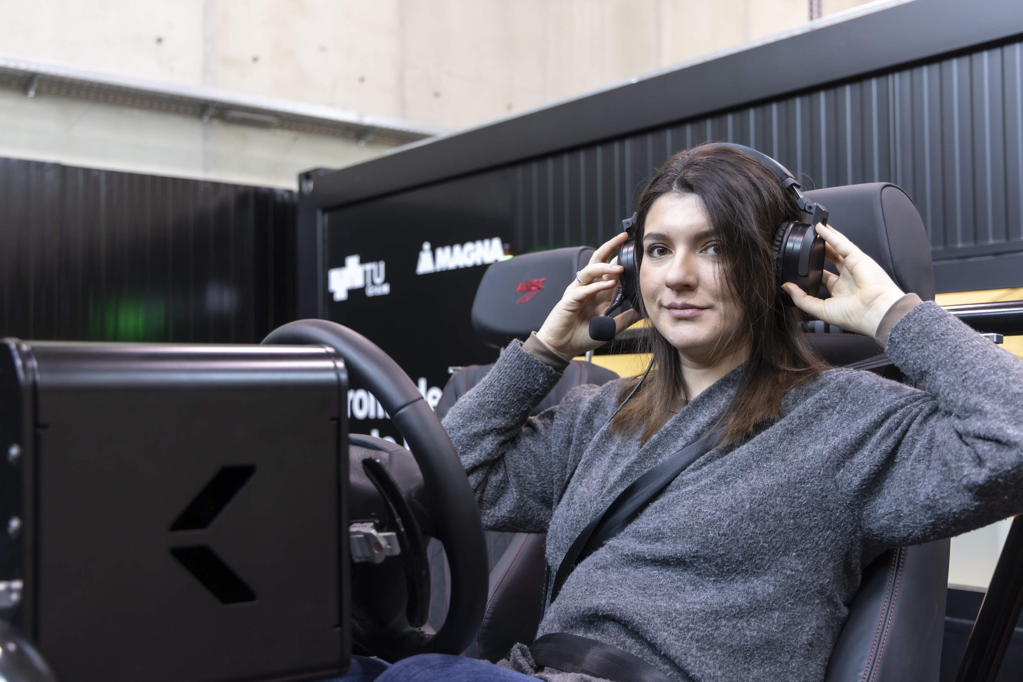A woman sits in a cockpit behind a steering wheel and puts on headphones.
