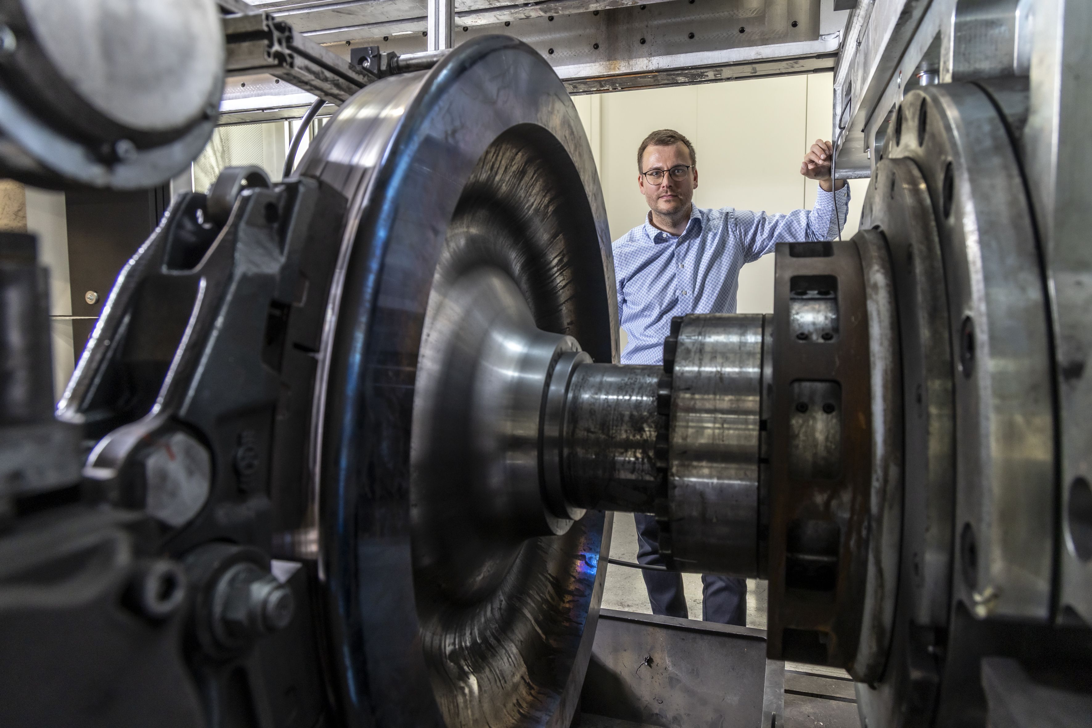 Ein großes kreisrundes Metallobjekt, seitlich dahinter ein ernst blickender Mann mit Brille.
