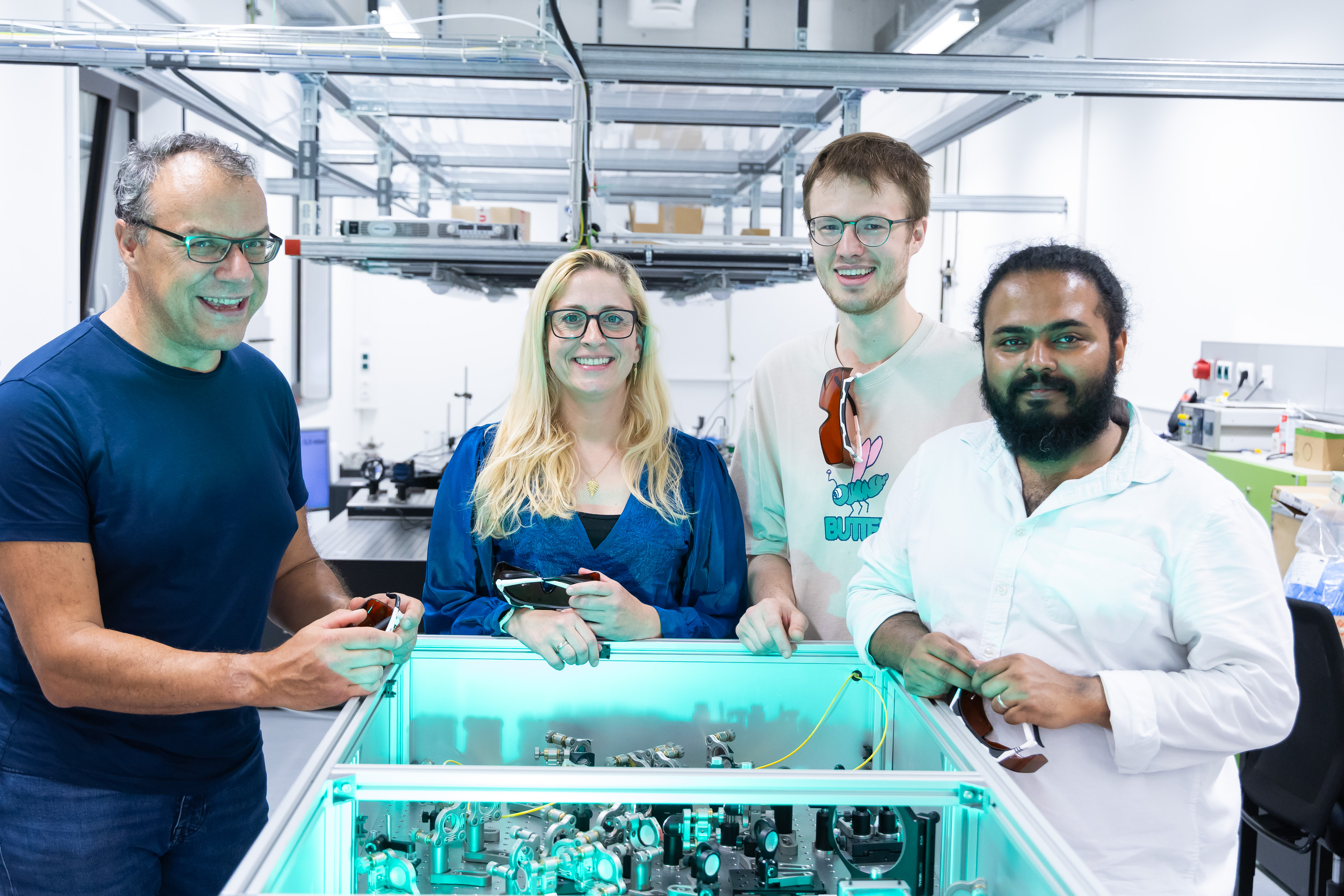Four people – three men and a woman – are standing around a device fitted with optical lenses.