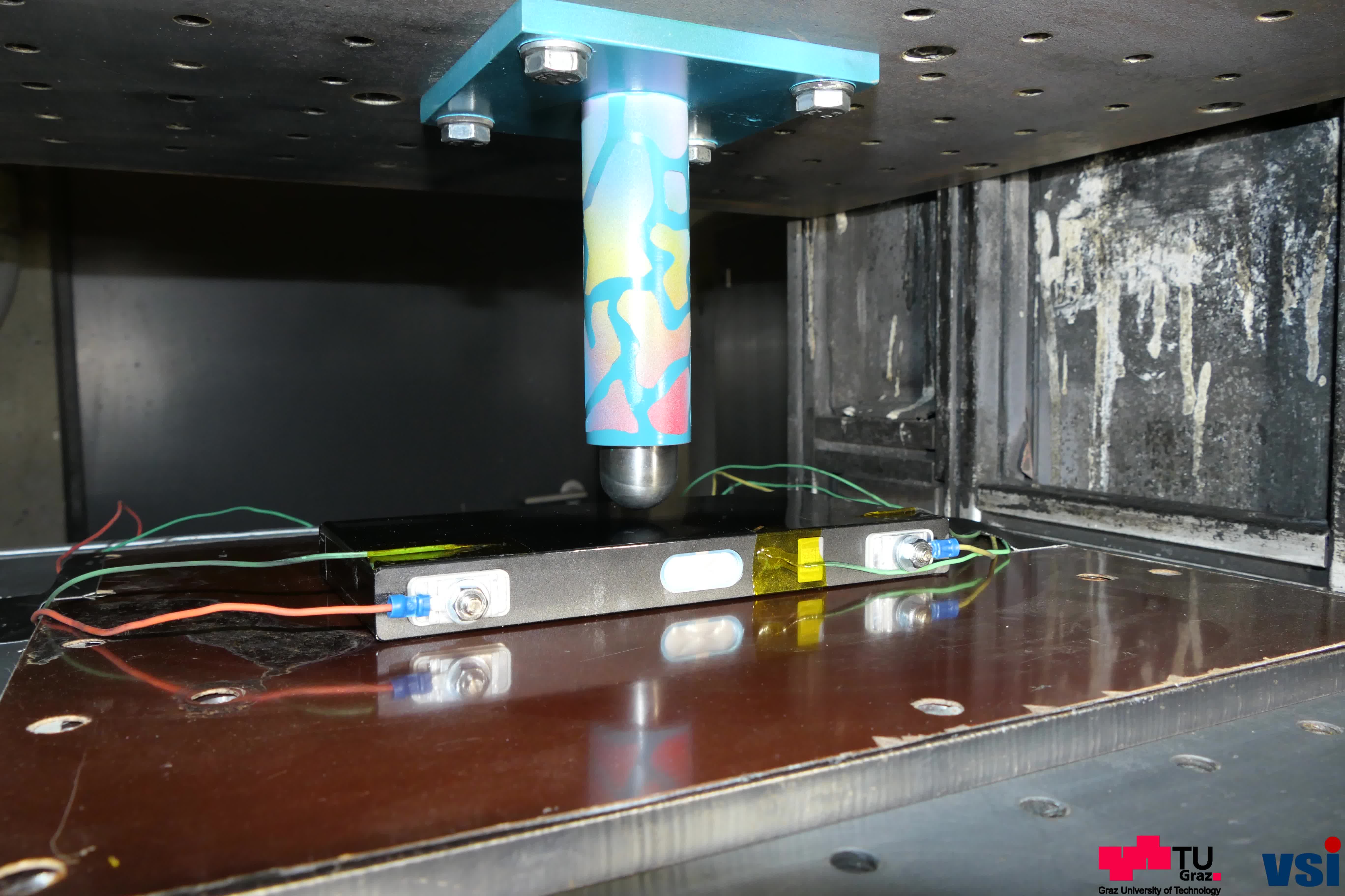 In a machine, a cylinder is pressed onto a battery pack to test its load-bearing capacity.