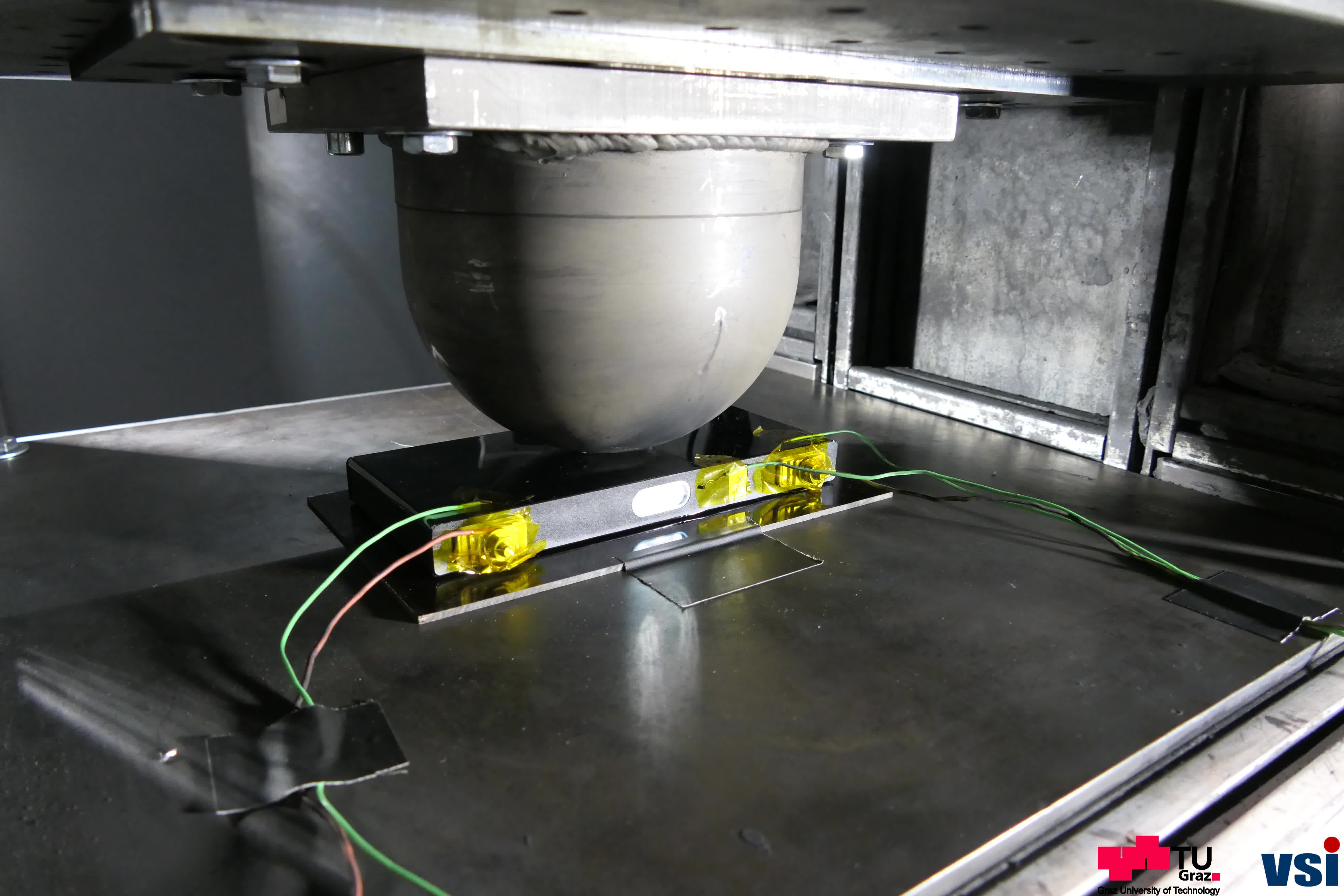 In a machine, a hemisphere is pressed onto a battery pack to test its load-bearing capacity.