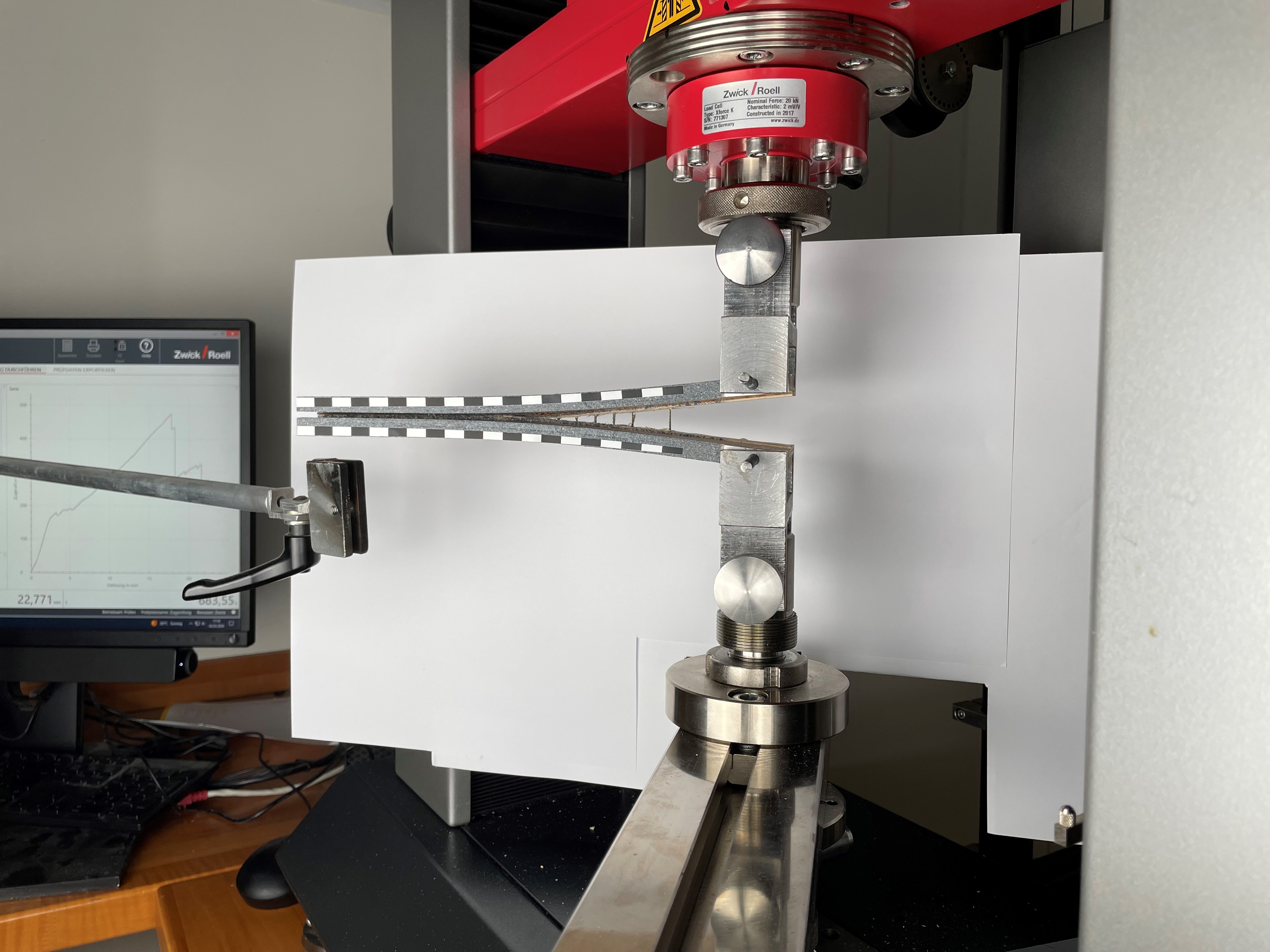 Eine Maschine zieht zwei Stücke Holz auseinander. Auf der rechten Seite sind sie bereits getrennt, auf der linken Seite halten sie noch zusammen.