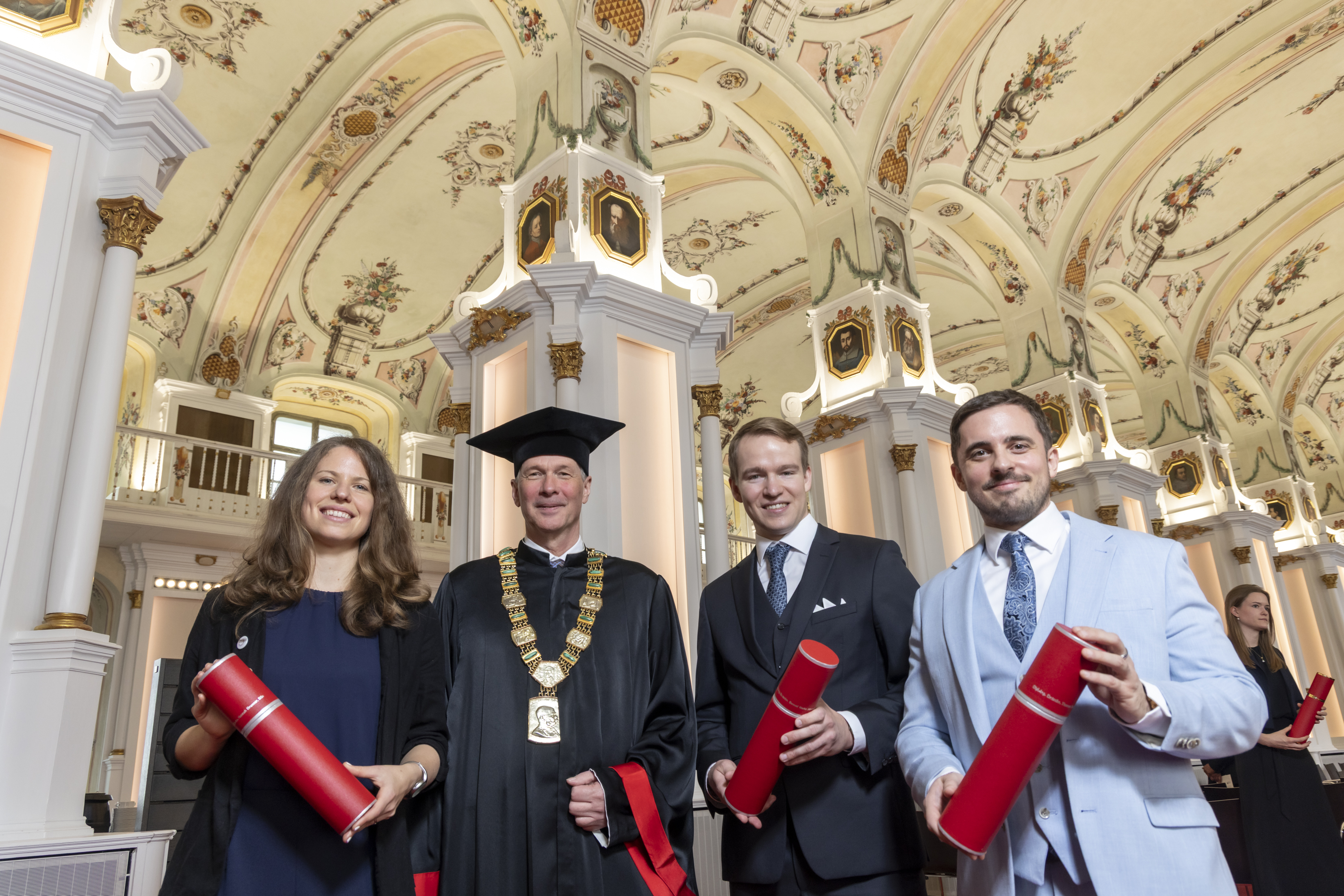 Vier Personen in festlicher Kleidung blicken in die Kamera. Drei von ihnen halten eine rote Roller in der Hand.