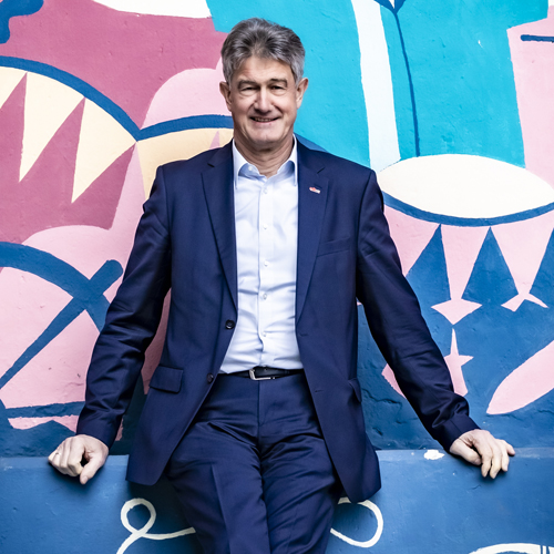 Man in a blue suit is sitting in front of a colourfully painted wall