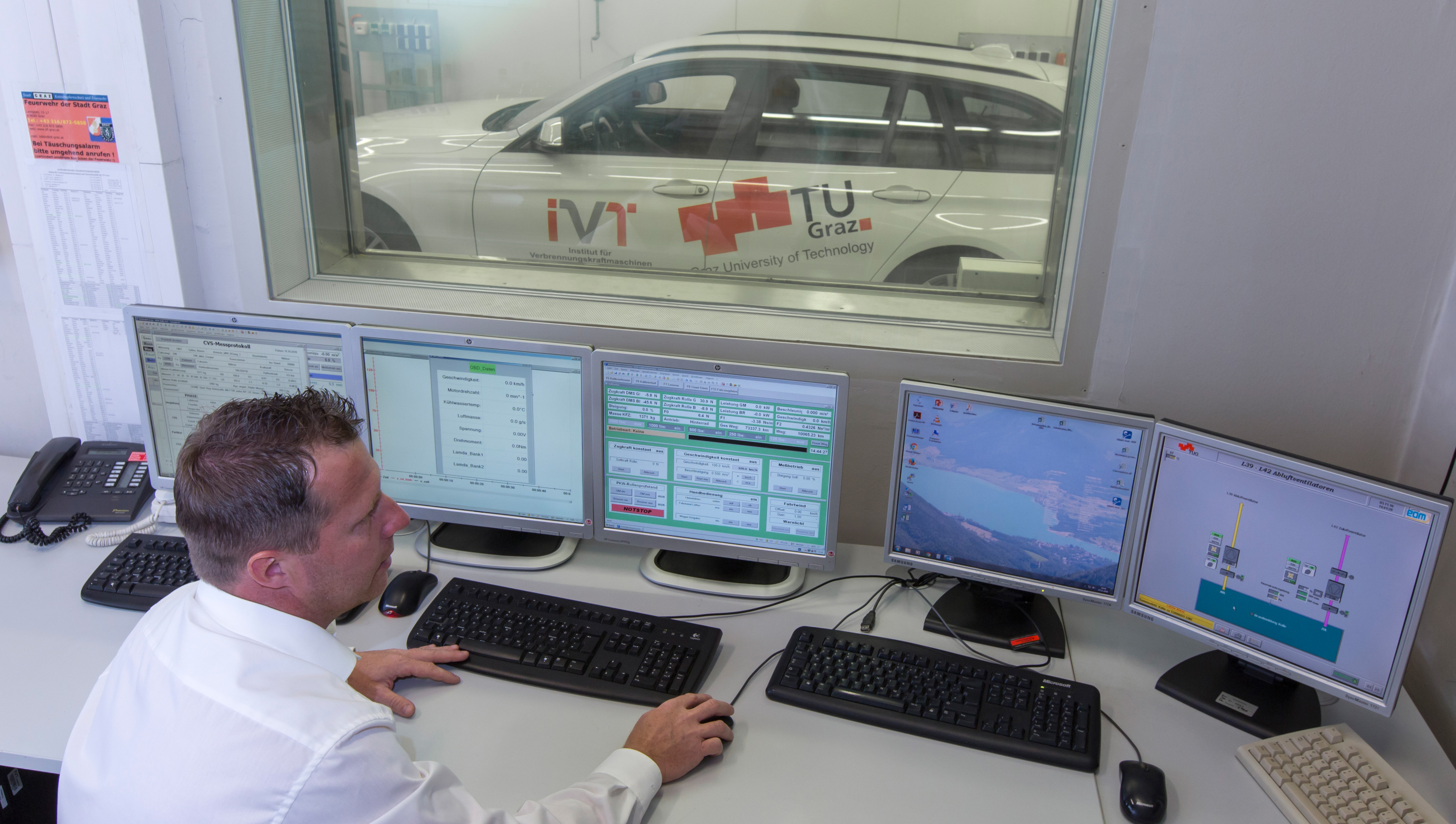Ein Herr im weißen Hemd beobachtet fünf Bildschirme und im Hintergrund durch ein Fenster ein weißes Auto