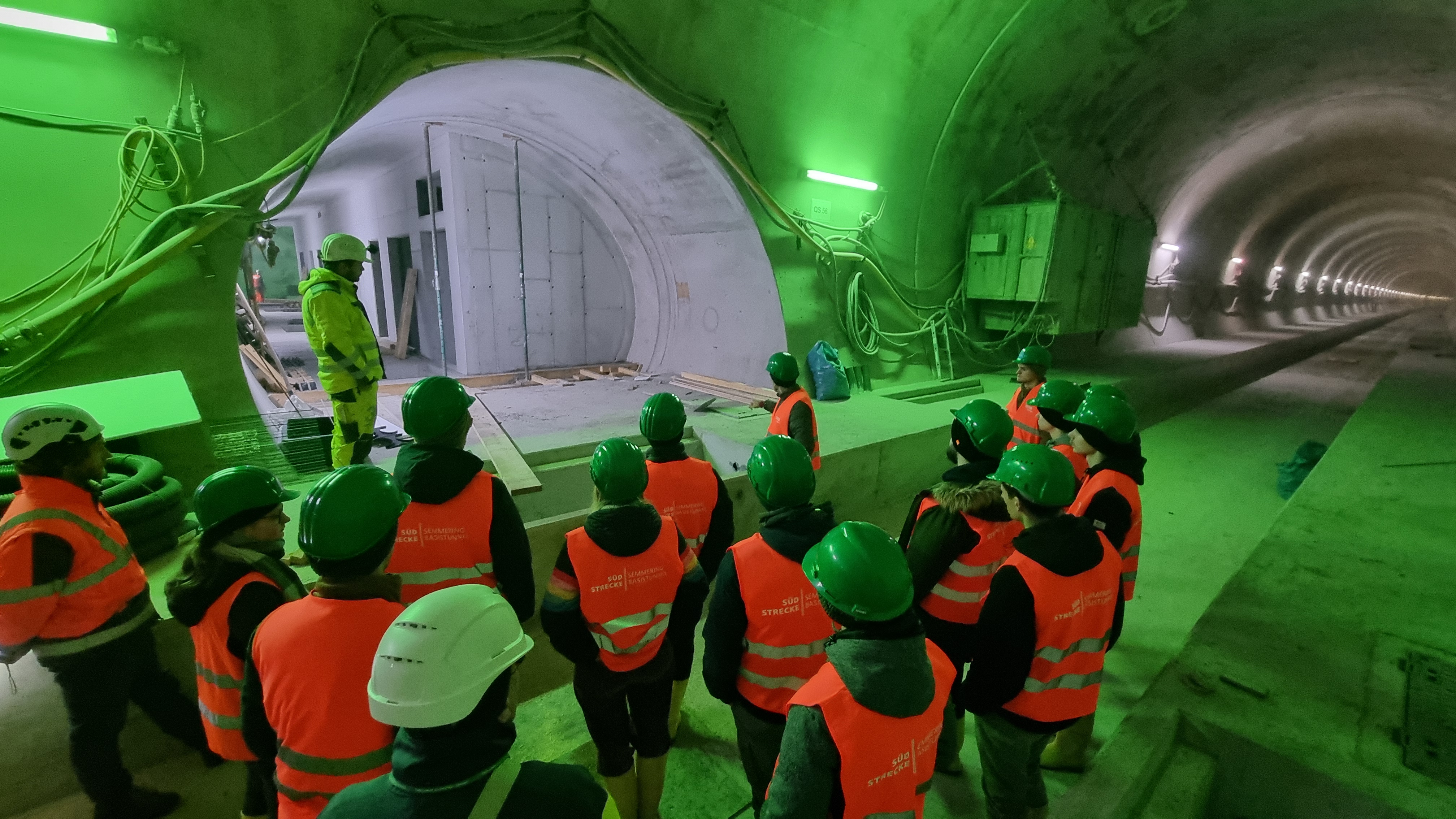 A group of people are standing in a tunnel tube, which is illuminated in green.