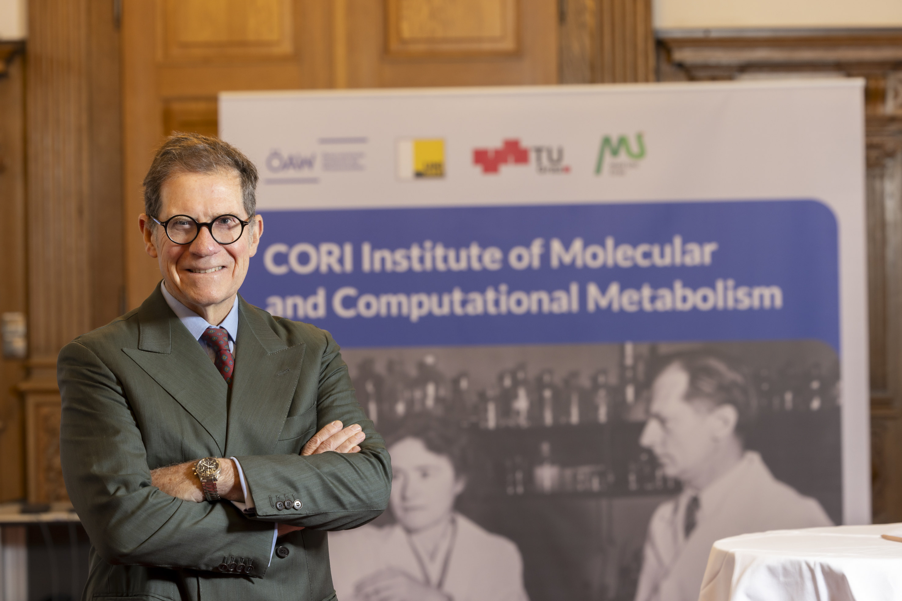 Ein Mann in einem Anzug lächelt in die Kamera. Er hat die Arme vor seiner Brust verschränkt.