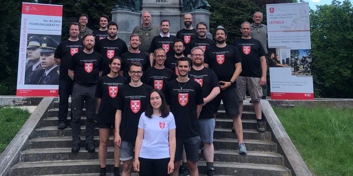 Teilnehmende am Kurs „Angewandtes Führungsverhalten in der Digitalen Transformation“ stehen auf Stufen aufgereiht im Park der MILAK, 2 Rollups der MILAK sind im Hintergrund zu sehen