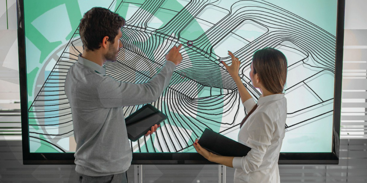 Two young people stand in front of a large screen and point to a graphic.